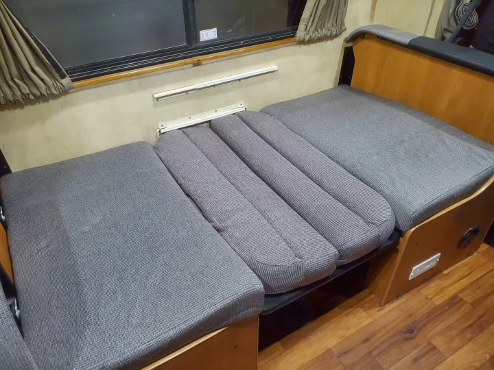 RV rental interior showing a convertible gray cushioned dinette area unfolded into a sleeping bed near a window.. Thor Majestic 2014
