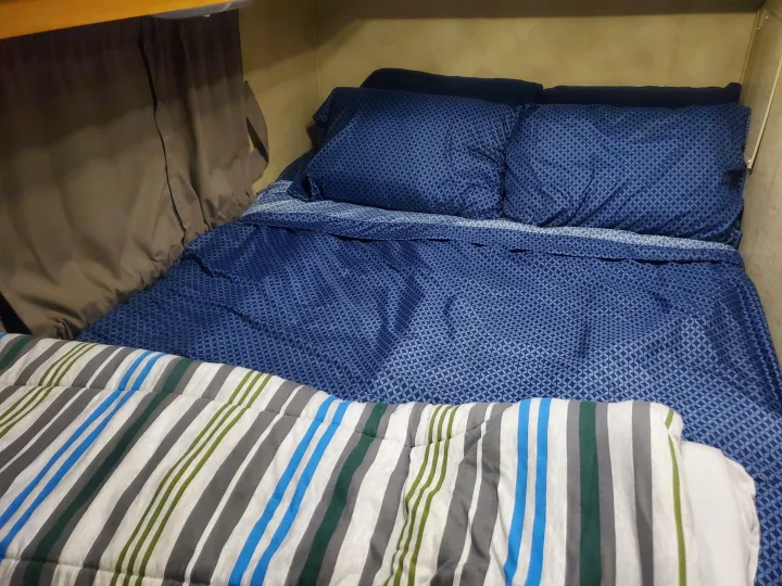 Cozy RV rental bed with blue patterned bedding and a striped comforter, ready for your travels.. Thor Majestic 2014