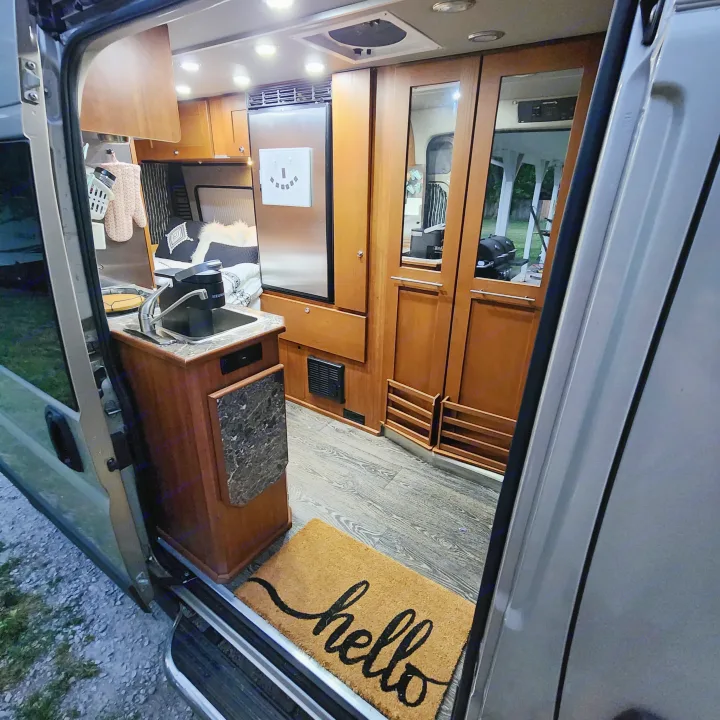 Spacious rv rental interior features warm wood cabinetry, a kitchen with a Keurig, fridge, and a welcoming 'hello' mat at the door.. Roadtrek Roadtrek Class B 2017