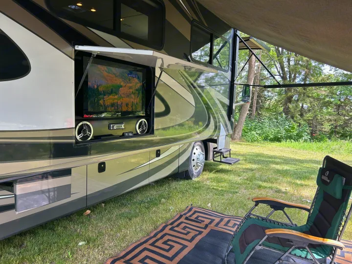 RV rental with outdoor TV, stereo, and speakers open on its side, ready for campsite entertainment with a chair.. Fleetwood Expedition 38B 2011