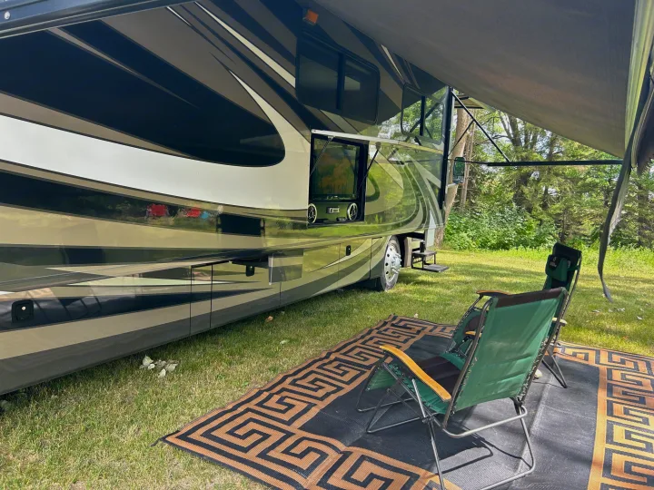 This RV rental is set up for outdoor living, featuring an extended awning, two green chairs, and a mat on the grass.. Fleetwood Expedition 38B 2011