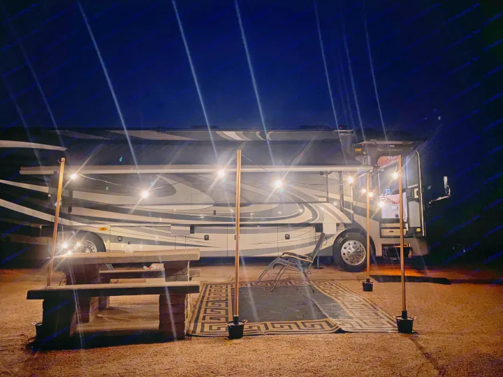 Enjoying an RV rental at night! Cozy outdoor setup with string lights, a picnic table, and rug beside the motorhome.. Fleetwood Expedition 38B 2011