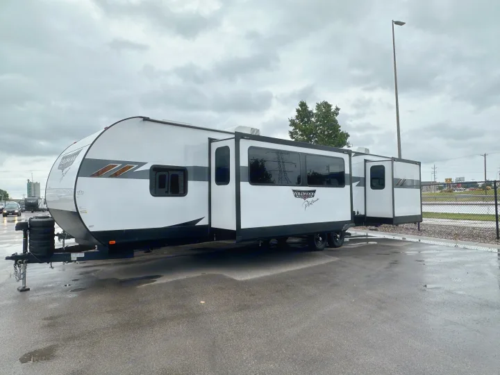 White Wildwood Platinum travel trailer, a premium RV rental, parked on wet asphalt under a cloudy sky.. Forest River Wildwood 2023
