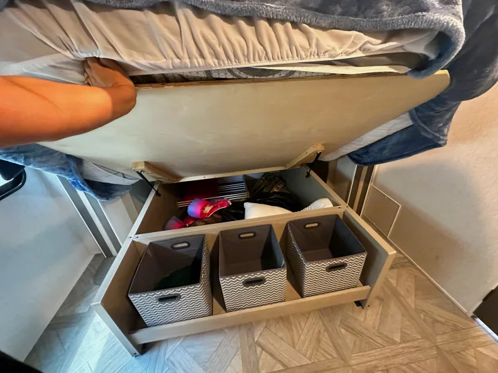 An RV rental bed lifts to reveal spacious under-bed storage, complete with organizational bins and various items.. Forest River Wildwood 2023