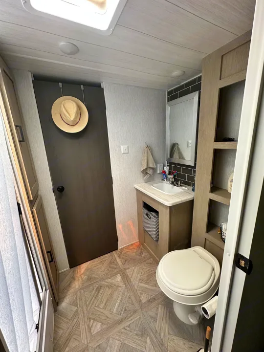 RV rental bathroom features a toilet, vanity, mirror, and stylish patterned wood-look floor.. Forest River Wildwood 2023