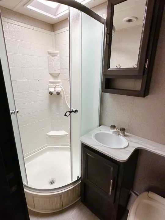 This RV rental's bathroom includes a functional corner shower, vanity with sink, and mirrored cabinet, optimized for travel.. Dutchmen Kodiak Ultimate 2018
