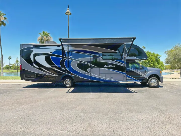 Blue and gray 'Four Winds' motorhome RV rental with extended awning and slide-out on a sunny day.. Thor Four Winds 2017