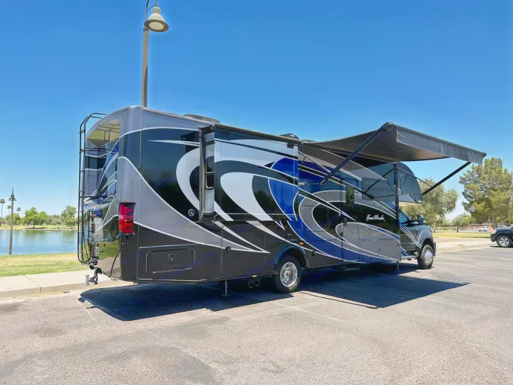 Stylish black, blue, and gray motorhome RV rental parked by a lake, awning extended, under a clear sky.. Thor Four Winds 2017