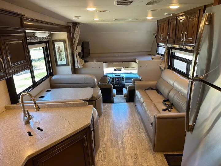 Experience this comfortable RV rental interior: kitchen, dining, sofa, driver's area, and over-cab bunk. Perfect for travel!. Thor Four Winds 2017