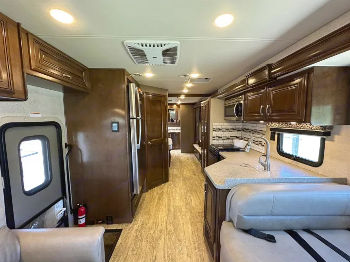 Spacious RV rental interior featuring a well-equipped kitchen with a sink, microwave, fridge, and dinette seating.. Thor Four Winds 2017