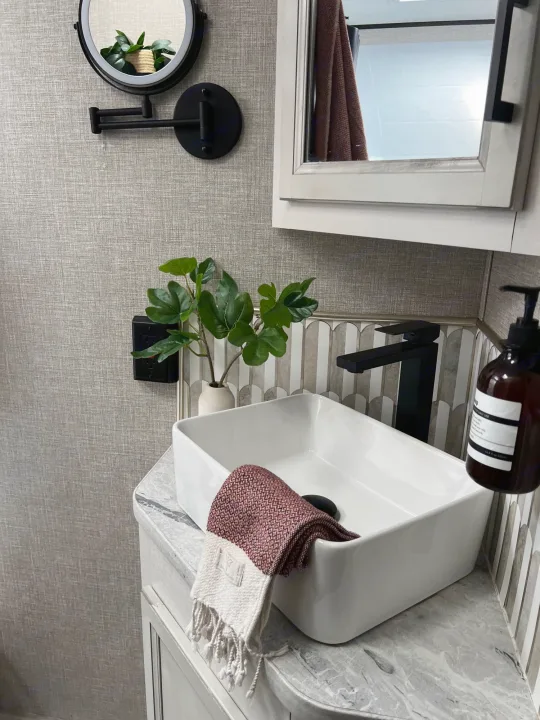 Explore this modern RV rental bathroom: vessel sink, black faucet, plant, and lighted mirror. Clean design with textured walls.. Jayco Featherlight SLX8 2022