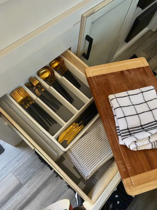 Inside an RV rental kitchen: organized drawer with black & gold flatware, plus a wooden cutting board & folded towels.. Jayco Featherlight SLX8 2022