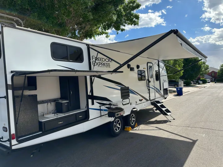 RV rental: A white travel trailer with its side awning extended and an outdoor kitchen revealed.. Forest River Coachmen Freedom Express Ultra Lite 2022