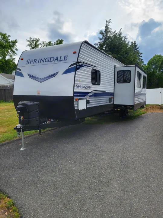 This white and gray Springdale travel trailer, ready for an rv rental, is parked outdoors with its slide-out extended.. Keystone RV Springdale 2022