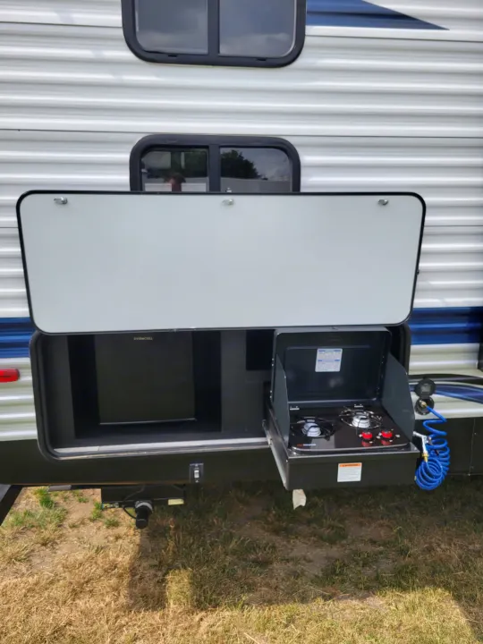 RV rental showing its outdoor kitchen: a mini-fridge, two-burner stove, and sprayer hose.. Keystone RV Springdale 2022