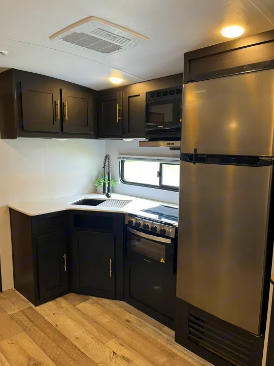 RV rental's modern kitchen: black cabinets, white counters, stainless steel fridge, oven, microwave & sink.. Keystone RV Springdale 2022