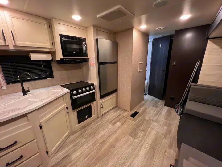 Modern RV rental kitchen featuring light cabinetry, microwave, fridge, stove, sink, and wood-look floor. Compact, functional design.. Jayco Jay Flight 2023