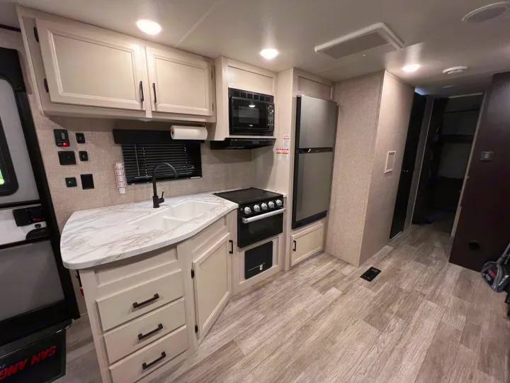 This rv rental features a modern, clean kitchen with light cabinets, a marble-look counter, sink, stovetop, microwave, and fridge.. Jayco Jay Flight 2023