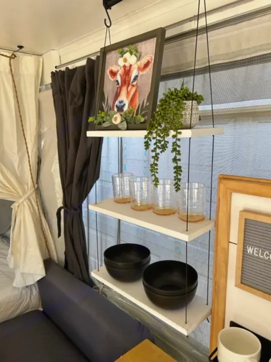 Cozy RV rental interior featuring decorative shelves with a cow picture, plants, glasses, and black bowls.. Coleman Frontier 1993