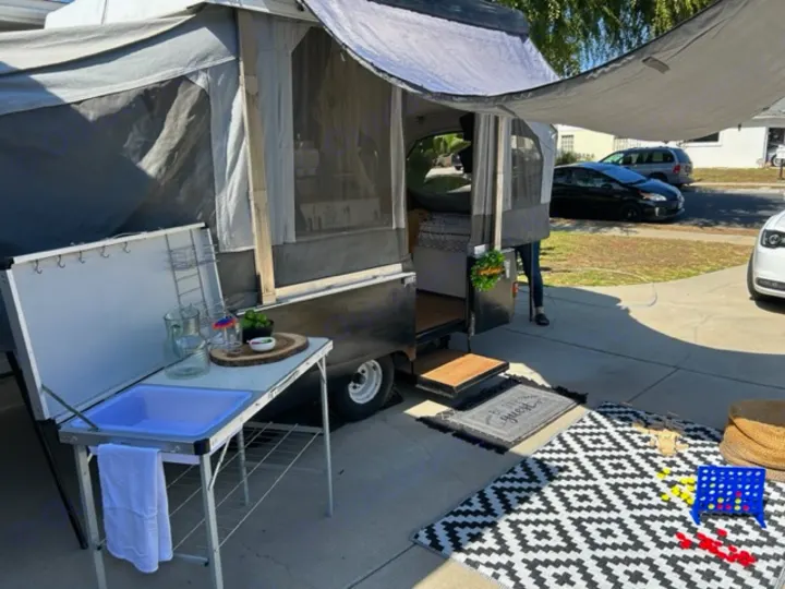 Cozy pop-up rv rental setup with outdoor kitchen, games, and inviting patio space. Perfect for your next adventure.. Coleman Frontier 1993