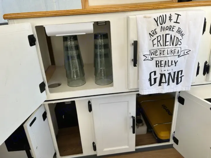 RV rental: Open compact kitchen area, with stacked glasses, hidden storage, and a yellow 'Martin' case. Towel reads 'SMALL GANG'.. Coleman Frontier 1993