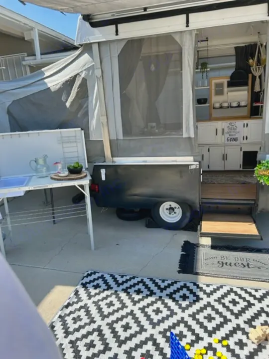 An RV rental, a pop-up camper, fully set up with an outdoor kitchen, patio rug, and interior cabinets visible.. Coleman Frontier 1993