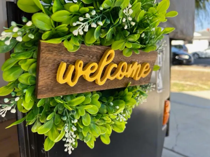 A detailed view of an artificial green wreath with a yellow 'welcome' sign, adorning an RV rental. An inviting outdoor accessory.. Coleman Frontier 1993