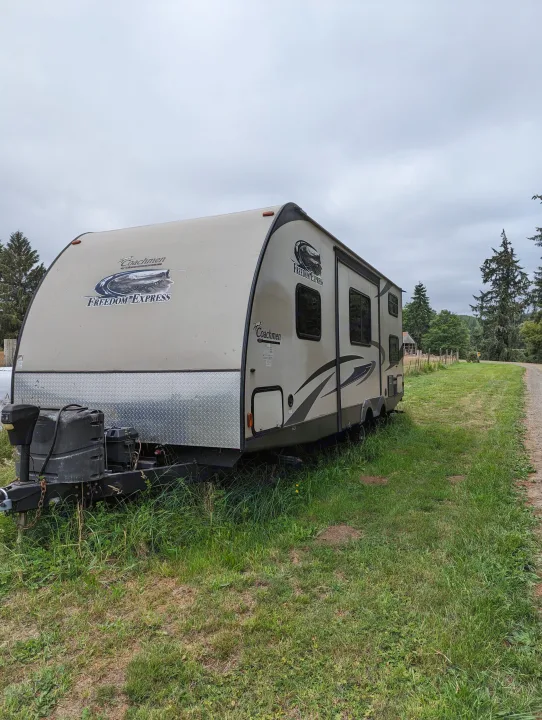 Coachmen Freedom Express RV rental parked in a grassy, rural setting next to a dirt road under an overcast sky.. Coachmen Freedom Express 2015