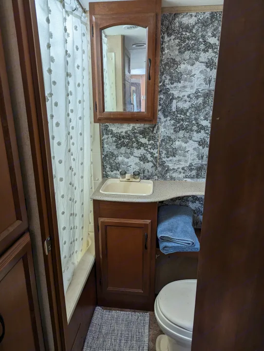 Stylish RV rental bathroom: white shower, sink, wood vanity, toilet, and decorative toile wallpaper.. Coachmen Freedom Express 2015