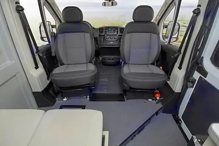 Inside an RV rental: front cabin with two swiveling seats & dashboard, leading to the rear living space. Perfect for travel!. Winnebago Solis PX 2024