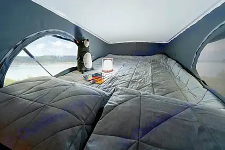 Interior of a cozy RV rental pop-top bed with a window view of a lake, featuring a plush toy and lamp.. Winnebago Solis PX 2024