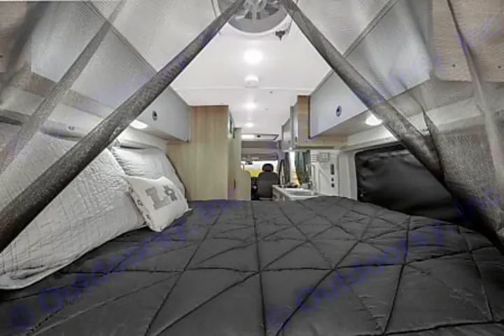 Experience comfort in this RV rental: a large, dark bed framed by a mesh net, looking towards the kitchen and cab.. Winnebago Solis PX 2024