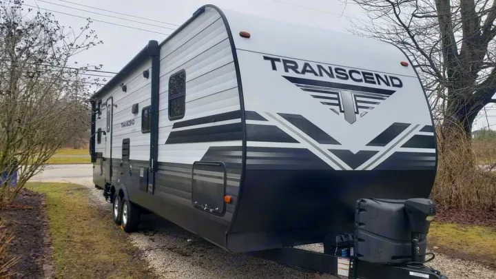 White and black Transcend travel trailer RV rental, ready for your next trip. Parked on a gravel lot.. Grand Design Transcend 2019