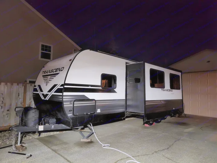 White and black travel trailer (RV) parked in a driveway at night.. Grand Design Transcend 2019