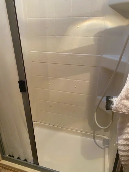 White compact shower stall in an RV rental, featuring a sliding glass door, handheld showerhead, and towel.. Jayco Redhawk 2016