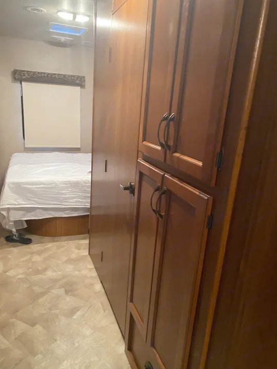 Neatly kept interior of an RV rental featuring a cozy bed with white sheets, warm wooden cabinets, and light patterned flooring.. Jayco Redhawk 2016