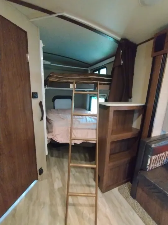 Cozy RV rental interior with bunk beds, a ladder to the upper bunk, wooden cabinetry, and windows, providing family sleeping space.. Dutchmen Aerolite 28dbhs 2017