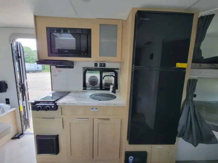 RV rental interior featuring a modern compact kitchen with microwave, fridge, stovetop, sink, and bunk beds.. Forest River Salem FSX 2023
