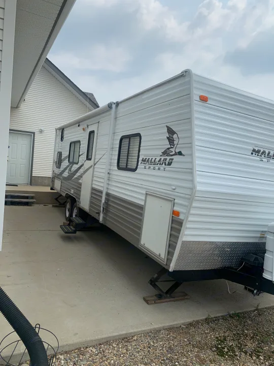White Mallard Sport travel trailer/RV parked on concrete beside a house, with leveling jacks, suitable for rv rental.. Fleetwood Mallard 2008