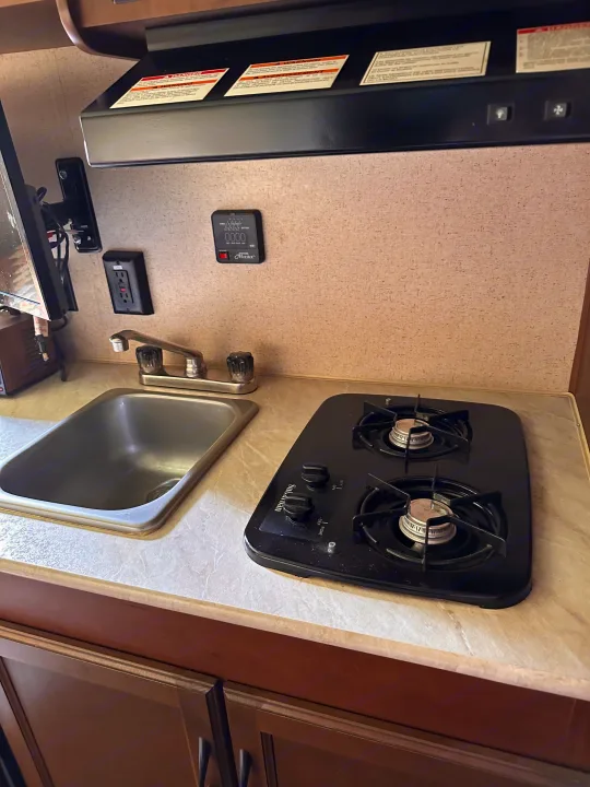 Explore this practical rv rental kitchen setup, complete with a two-burner stovetop, sink, and essential monitoring display.. Jayco Jay Flight SLX 2015
