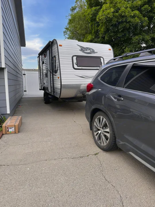 A white travel trailer, often used for RV rental, is hitched to a gray SUV on a driveway.. Jayco Jay Flight SLX 2015