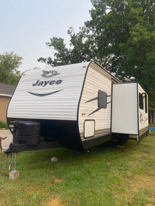 White Jayco travel trailer, an ideal rv rental, parked on grass. Its large slide-out is extended, offering extra space.. Jayco Jay Flight SLX 2017