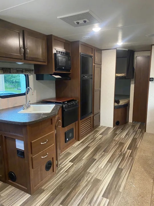 Spacious RV rental interior highlighting a full kitchen with dark wood cabinets, modern appliances, and convenient bunk beds.. Jayco Jay Flight SLX 2017
