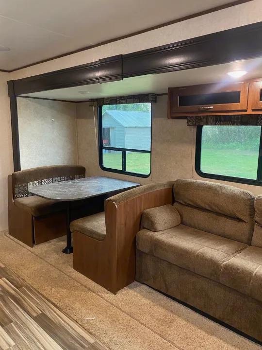 Inside a cozy RV rental: a comfy dinette with a gray table and a brown sofa for relaxing. Views outside from large windows.. Jayco Jay Flight SLX 2017