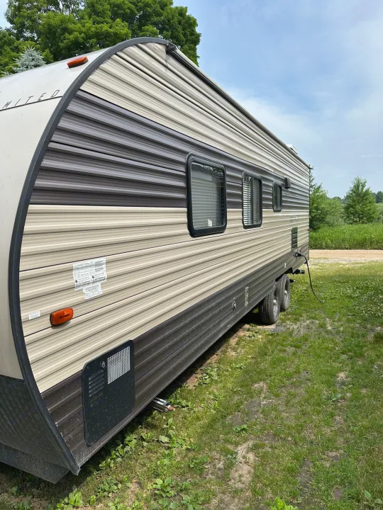 Side view of a striped travel trailer for RV rental, parked on green grass under a bright sky.. grey wolf bunkhouse 2018