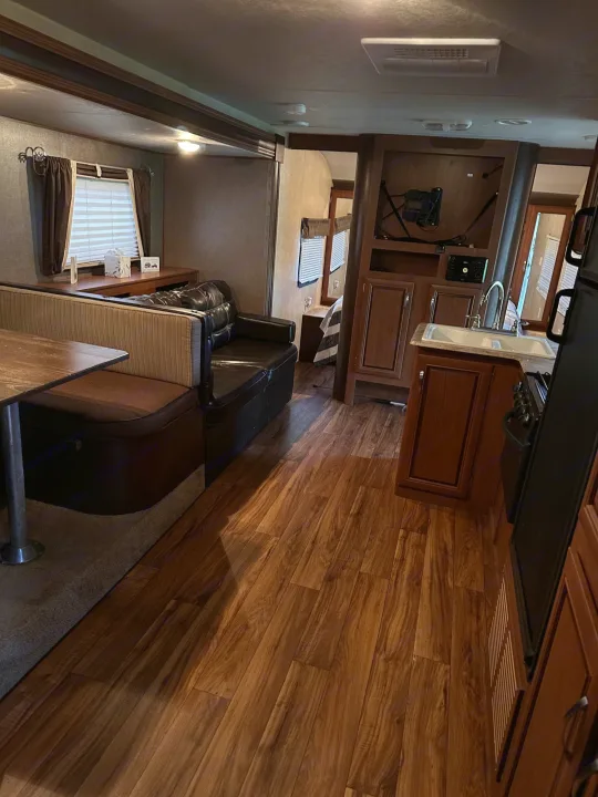 Inviting RV rental interior: wood-look floors, dinette, comfortable couch, and functional kitchen with sink & stove.. Forest River Wildwood X-Lite 2015