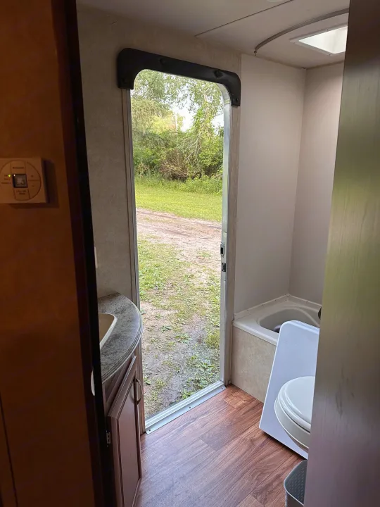Inside an RV rental: Bathroom with sink, shower, toilet, and an open door view to nature.. Forest River Wildwood X-Lite 2015