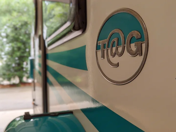 A distinctive white and teal T@G RV rental, featuring its unique metallic logo and striped side. Ideal for memorable travels.. nuCamp T@G 2017