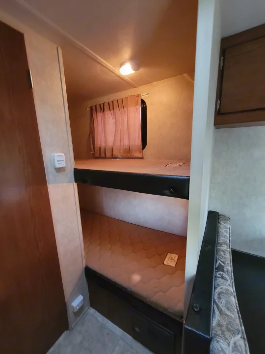 Cozy RV rental interior featuring comfortable bunk beds with a window and curtains, along with a thermostat on the wall.. Forest River Wildwood X-Lite 2014