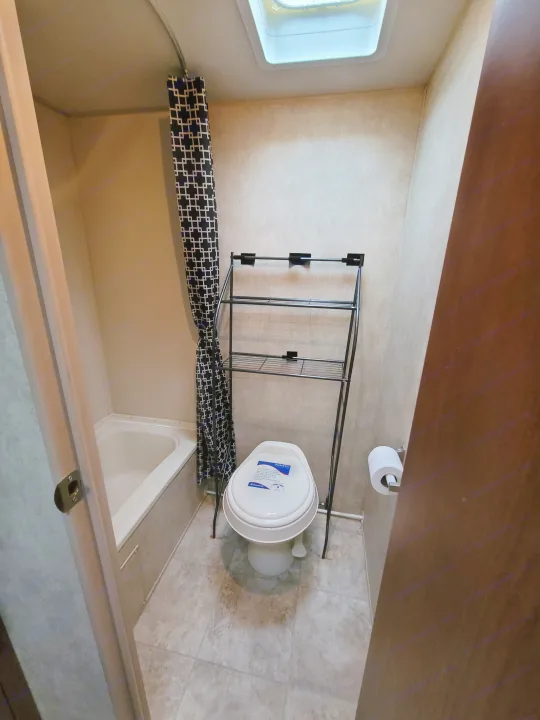 Compact RV rental bathroom featuring a tub, Dometic toilet with storage, and overhead skylight.. Forest River Wildwood X-Lite 2014